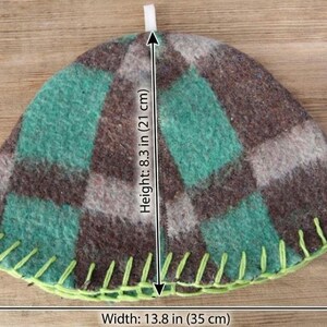 Puede incluir: Un calentador de t&eacute; hecho a mano con un patr&oacute;n de cuadros en tonos verdes, marrones y grises. El calentador mide 21 cm de alto y 35 cm de ancho, con un borde cosido en verde lima y un lazo blanco en la parte superior.