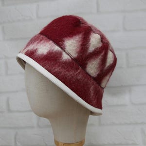 May include: A red and white patterned bucket hat with a white brim. The hat is made of a fuzzy material and is displayed on a mannequin head. The hat has a stitched seam around the top.