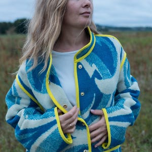 May include: A blue and white patterned coat with yellow trim and gold buttons. The coat has a unique design and is worn by a person in a field. The coat's design is a mix of blue and white, with yellow trim outlining the edges.
