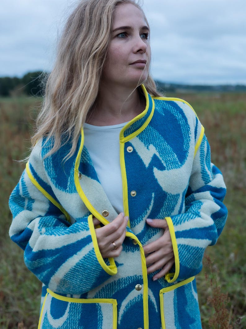 May include: A blue and white patterned coat with yellow trim and gold buttons. The coat has a unique design and is worn by a person in a field. The coat's design is a mix of blue and white, with yellow trim outlining the edges.