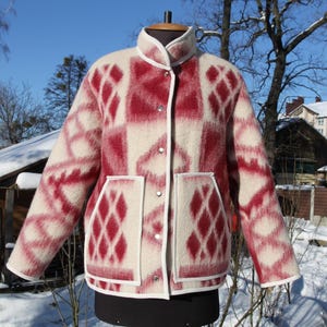 Puede incluir: Chaqueta estampada en crema y rojo con diseño de diamantes. La chaqueta tiene cuello alto, dos bolsillos delanteros y botones plateados. Ribetes blancos acentúan el cuello, los bolsillos y los bordes de la chaqueta. La chaqueta se exhibe en un maniquí.
