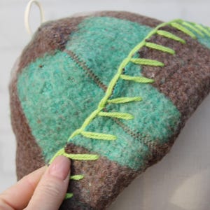 Puede incluir: Un sombrero hecho a mano con un patr&oacute;n de cuadros en tonos marrones y verde azulado. El sombrero presenta costuras de color verde brillante a lo largo del borde. El sombrero est&aacute; hecho de un material suave y texturizado.