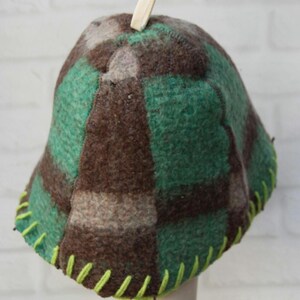 Puede incluir: Sombrero hecho a mano con un dise&ntilde;o a cuadros verdes, marrones y grises. Est&aacute; hecho de lana afieltrada con una copa redondeada y un ala. El sombrero tiene un ribete cosido verde brillante en la base y un peque&ntilde;o lazo blanco roto en la parte superior.