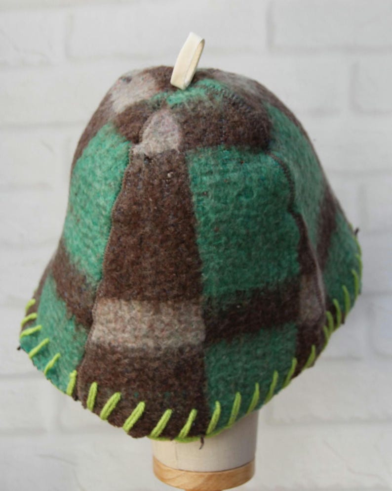 Puede incluir: Sombrero hecho a mano con un dise&ntilde;o a cuadros verdes, marrones y grises. Est&aacute; hecho de lana afieltrada con una copa redondeada y un ala. El sombrero tiene un ribete cosido verde brillante en la base y un peque&ntilde;o lazo blanco roto en la parte superior.