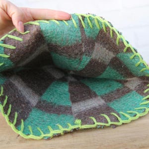 Puede incluir: Una bolsa hecha a mano con un dise&ntilde;o de cuadros verdes y marrones. Los bordes est&aacute;n cosidos con hilo verde ne&oacute;n brillante. El interior de la bolsa es visible, mostrando la tela de cuadros. La bolsa est&aacute; hecha de un material suave y afieltrado.