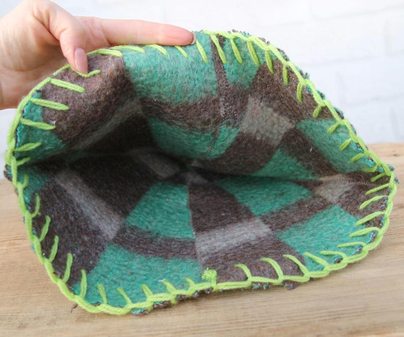 Puede incluir: Una bolsa hecha a mano con un dise&ntilde;o de cuadros verdes y marrones. Los bordes est&aacute;n cosidos con hilo verde ne&oacute;n brillante. El interior de la bolsa es visible, mostrando la tela de cuadros. La bolsa est&aacute; hecha de un material suave y afieltrado.