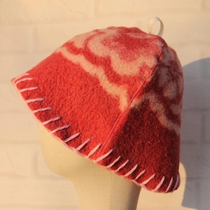 Peut inclure: Un chapeau en feutre rouge avec un motif tourbillonnant blanc et une boucle blanche sur le dessus. Le chapeau a une bordure cousue rose autour du bord. Le chapeau est présenté sur une tête de mannequin.