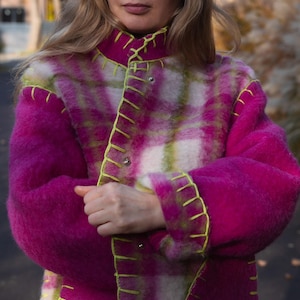 Puede incluir: Un abrigo vibrante y difuso con un estampado de cuadros en rosa, blanco y verde. El abrigo presenta costuras y cuello de color amarillo brillante. El abrigo tiene un cuello alto y cierres de botones plateados.