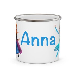 May include: White enamel mug with a silver rim featuring the name "Anna" in blue. The mug is decorated with cartoon images of Anna and Elsa from the movie Frozen. A fun and colorful gift for fans of the animated film.