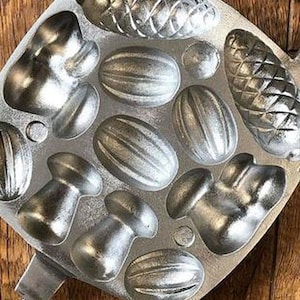 May include: A silver metal mould with 12 different shapes for making candy or chocolate. The shapes include mushrooms, pine cones, and various nuts.