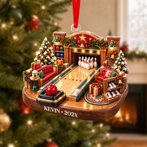 May include: A decorative Christmas ornament featuring a miniature bowling alley scene with a red bowling ball, white pins, red seating, and Christmas trees. The base is wood-toned with the text KEVIN 202X printed on the front, suspended by a red ribbon.