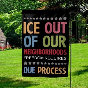 May include: Black garden flag with the text "ICE OUT OF OUR NEIGHBORHOODS FREEDOM REQUIRES DUE PROCESS" in colorful block letters. The flag is hanging on a black metal stand in a grassy yard with trees and a house in the background.