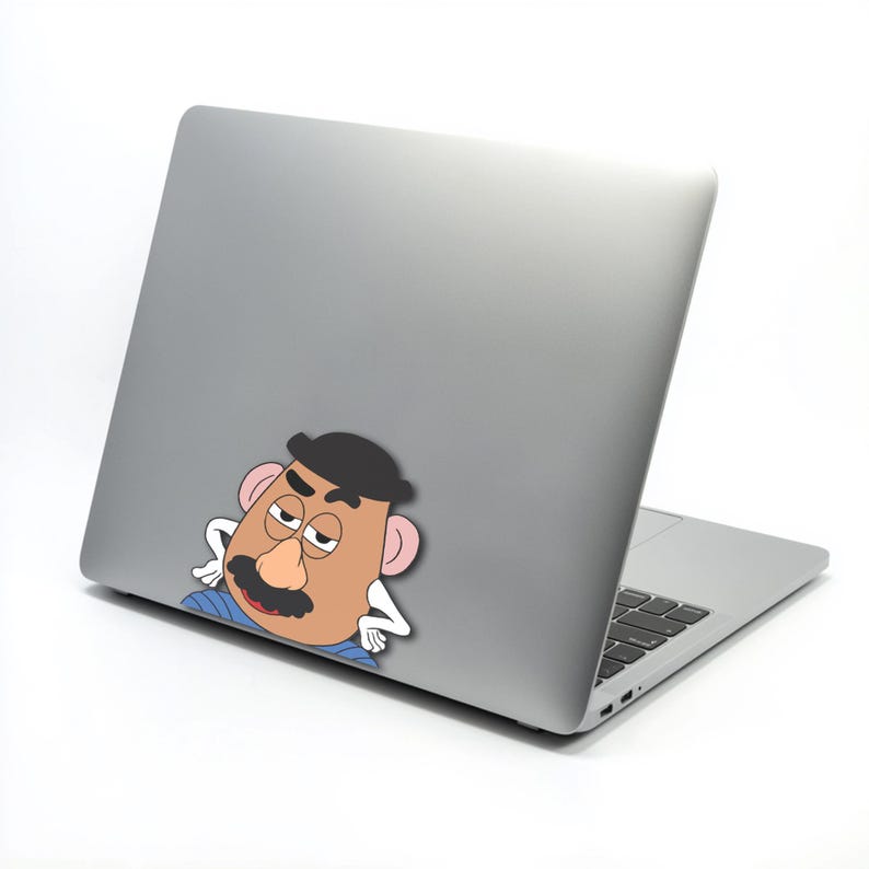 May include: A silver laptop with a Mr. Potato Head sticker on the back. The sticker shows a cartoon character with a tan face, black mustache and hat, and pink ears. The laptop is open, showing the keyboard.