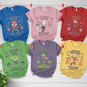 May include: Six colourful t-shirts featuring Marvel comic book characters. Each shirt has a different character design, including Spider-Man, Gwen, Hulk, Green Goblin, and Iron Man, with related text and graphics. The shirts are blue, pink, red, green, purple, and yellow.