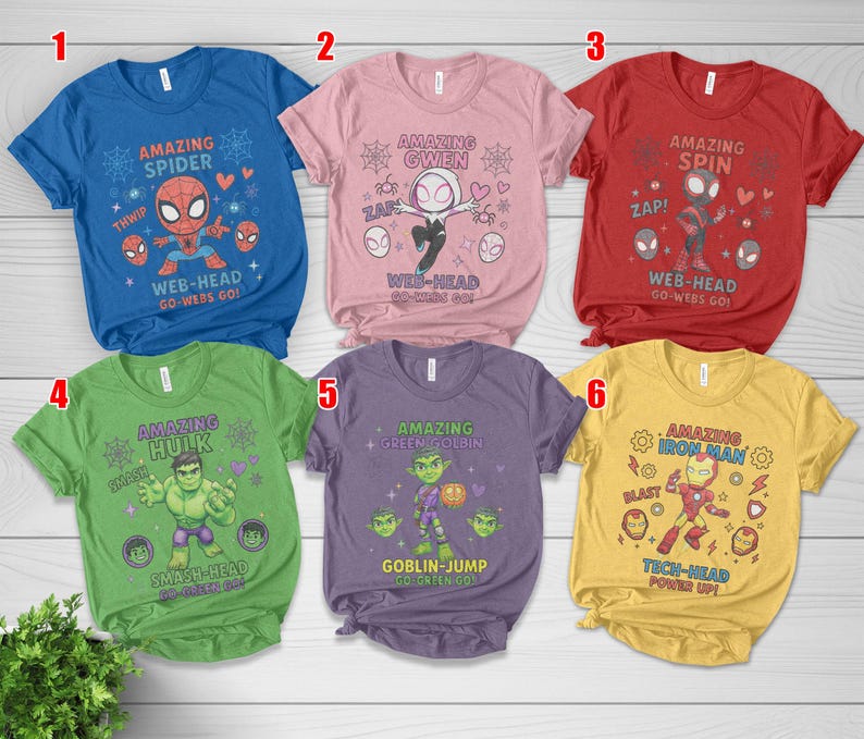 May include: Six colourful t-shirts featuring Marvel comic book characters. Each shirt has a different character design, including Spider-Man, Gwen, Hulk, Green Goblin, and Iron Man, with related text and graphics. The shirts are blue, pink, red, green, purple, and yellow.