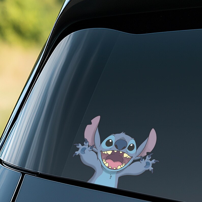 May include: A blue cartoon character sticker, featuring a wide-eyed, smiling alien with large ears and outstretched arms. The sticker is applied to a car window, with the background showing a blurred outdoor scene.