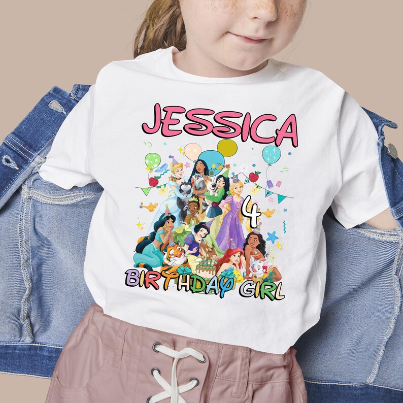 May include: White t-shirt featuring a colorful graphic of Disney princesses, the name "JESSICA", the number "4", and the words "BIRTHDAY GIRL". The design includes balloons and confetti.