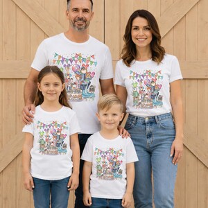 May include: A family of four wearing matching white t-shirts with a colorful birthday-themed graphic. The design includes cartoon animals, balloons, a cake, and the word "Name". The family is standing in front of a wooden door.