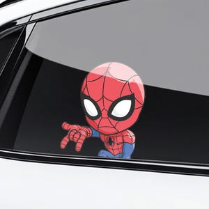 Pode incluir: Um adesivo do Homem-Aranha em estilo cartoon, com uma fantasia vermelha e azul e um padr&atilde;o de teia de aranha na cabe&ccedil;a. O adesivo &eacute; aplicado em um vidro de carro, com o personagem apontando para frente.