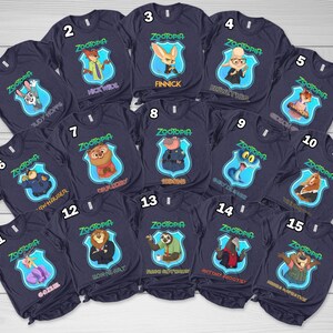 May include: A collection of fifteen dark navy blue t-shirts, each featuring a Zootopia character graphic inside a light blue shield emblem. The shirts are numbered one through fifteen and display names like Judy Hopps, Nick Wilde, and Flash.