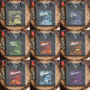 May include: Nine charcoal gray t-shirts with different cartoon car graphics. Each shirt features a car character's name, the year 2006, and the word "Rusteze". The cars are in various colors, including yellow, blue, purple, green, red, and orange.