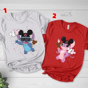 K&ouml;nnte beinhalten: Zwei kurz&auml;rmelige T-Shirts. Eines ist wei&szlig; mit einer blauen Zeichentrickfigur mit Sonnenbrille, schwarzem Hut und Luftballons und Eis. Das andere ist rot mit einer rosa Zeichentrickfigur, die Eis und Luftballons h&auml;lt.
