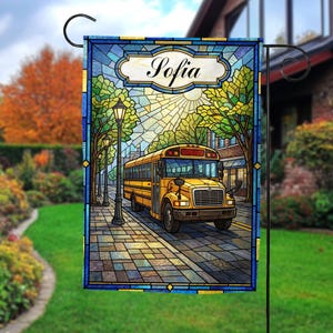 May include: A decorative garden flag featuring a yellow school bus driving down a city street. The flag has a stained-glass style design with the name "Sofia" at the top. The background includes trees, buildings, and a bright sun.