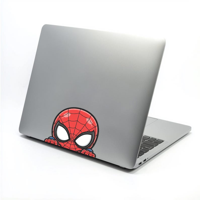 May include: A silver laptop with a red and black Spider-Man sticker peeking from the bottom. The sticker features the character's iconic mask with white eyes and a red web pattern.