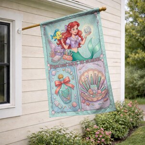 Puede incluir: Una bandera decorativa para exteriores con una sirena de pelo rojo y cola verde, sosteniendo un orbe brillante. La bandera tiene un fondo turquesa con las palabras "PRINCESS BACK TO SCHOOL". La bandera tambi&eacute;n presenta una concha con brochas de maquillaje.