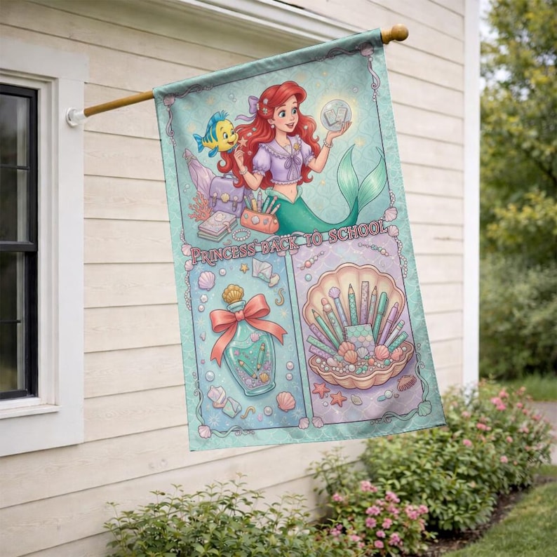 Puede incluir: Una bandera decorativa para exteriores con una sirena de pelo rojo y cola verde, sosteniendo un orbe brillante. La bandera tiene un fondo turquesa con las palabras "PRINCESS BACK TO SCHOOL". La bandera tambi&eacute;n presenta una concha con brochas de maquillaje.