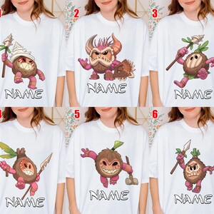 Puede incluir: Camisetas blancas con personajes de dibujos animados y la palabra "NAME" debajo. Los personajes son marrones, rosas y blancos, con varios accesorios y expresiones. Las camisetas se muestran en una persona.