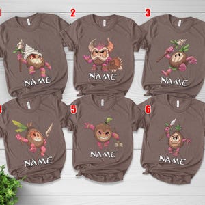 Puede incluir: Camisetas marrones con personajes de dibujos animados de coco en varias poses. Cada camiseta presenta un dise&ntilde;o de personaje diferente, con la palabra "NAME" impresa debajo. Las camisetas son de manga corta.