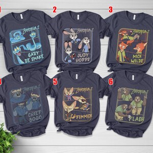 Pode incluir: T-shirts azul marinho com personagens de Zootopia 2. Cada camisa exibe um personagem ou grupo de personagens diferente dentro de uma moldura retangular. Personagens: Gary De Snake, Judy Hopps, Nick Wilde, Chief Bogo, Finnick e Flash.