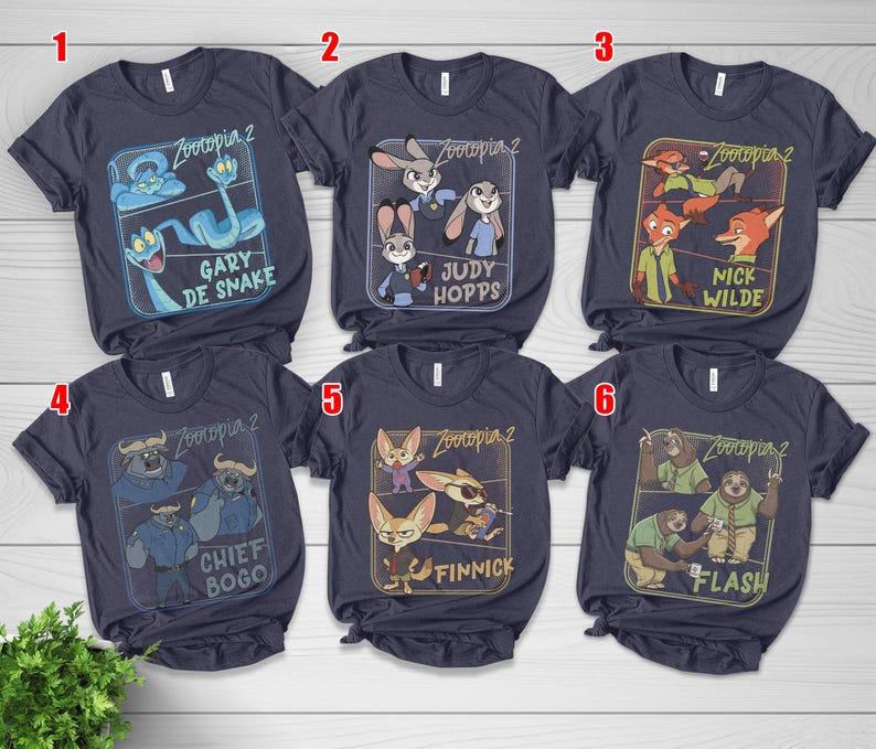 Pode incluir: T-shirts azul marinho com personagens de Zootopia 2. Cada camisa exibe um personagem ou grupo de personagens diferente dentro de uma moldura retangular. Personagens: Gary De Snake, Judy Hopps, Nick Wilde, Chief Bogo, Finnick e Flash.