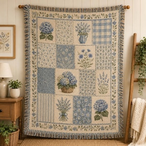 May include: A woven throw blanket featuring a patchwork design of blue and cream floral patterns, including hydrangea blossoms, lavender sprigs, and checkered squares, finished with a decorative floral border and fringed edges on all sides.