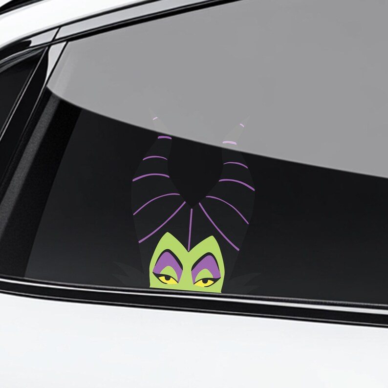 May include: A car window decal featuring a cartoon image of Maleficent, with her signature black horns with purple stripes, green face, and yellow eyes. The decal is visible through the car window.