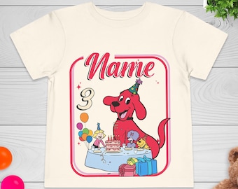 May include: A cream-colored short-sleeve t-shirt featuring a graphic of a red dog wearing a party hat next to a birthday cake, a child, and other dogs. The design includes the text Name and the number 3, surrounded by colorful balloons and gifts.