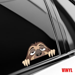 May include: A brown and tan sloth peeking out from behind a car window. The sloth has a sleepy expression and is holding onto the window frame with its white claws. The word "VINYL" is printed in red in the bottom right corner.