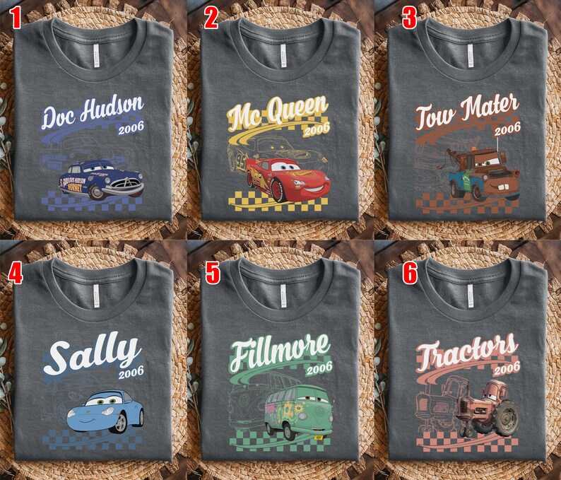 May include: A collection of six dark gray t-shirts featuring characters from the movie Cars. Each shirt displays a unique character name, the year 2006, a graphic of the character, and a checkered pattern at the bottom. Characters include Doc Hudson, Mc Queen, Tow Mater, Sally, Fillmore, and Tractors.