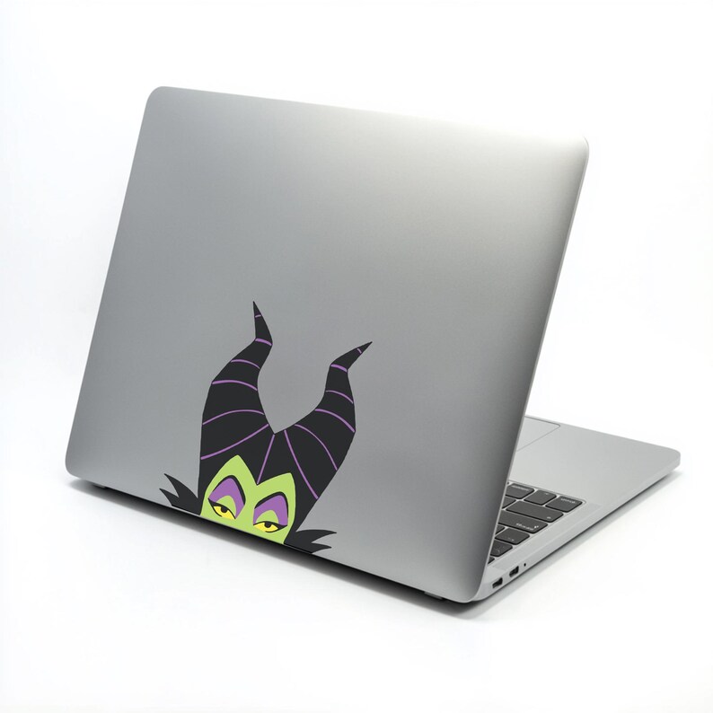 May include: A silver laptop with a black keyboard and a sticker featuring a cartoon character with black horns, green face, and yellow eyes. The sticker is on the back of the laptop.