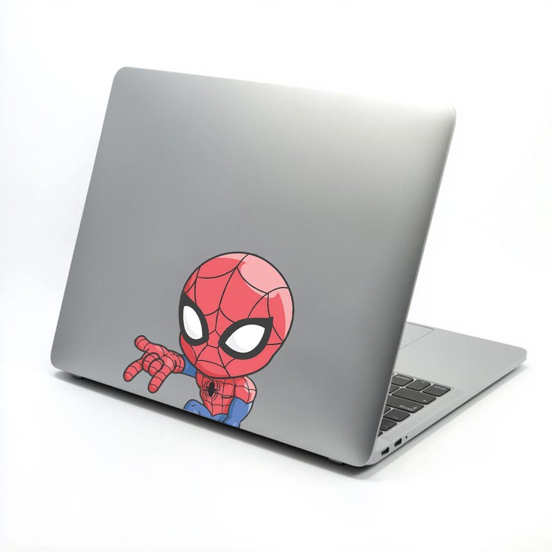 Pode incluir: Um adesivo de desenho animado do Homem-Aranha, em vermelho e azul, est&aacute; afixado na parte de tr&aacute;s de um laptop prateado. O adesivo apresenta a m&aacute;scara do Homem-Aranha com grandes olhos brancos e uma m&atilde;o estendida.