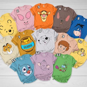 May include: A collection of thirteen short-sleeved t-shirts in various colors, each featuring a different character graphic from the Winnie the Pooh series, including Pooh, Piglet, Tigger, Eeyore, and a honey pot with the text HUNNY.