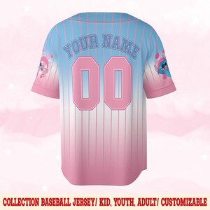 Pode incluir: Uma camisa de beisebol rosa e azul com listras brancas. A camisa tem "YOUR NAME" e "00" impressos nas costas. A camisa apresenta um personagem de desenho animado em cada manga.