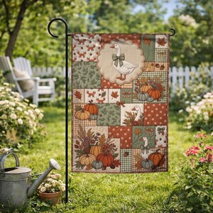 Pu&ograve; includere: Una bandiera da giardino rettangolare con un design patchwork che raffigura oche con fiocchi, zucche e foglie autunnali in tonalit&agrave; arancione, verde e crema. La bandiera &egrave; esposta su un supporto in metallo nero in un giardino.