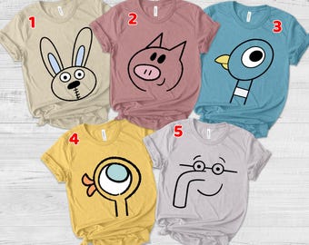 May include: Five short-sleeved crew neck t-shirts in beige, mauve, blue, yellow, and light gray. Each shirt features a simple black-lined cartoon character face: a rabbit, a pig, a blue bird, a yellow bird, and a person with glasses and a large nose.