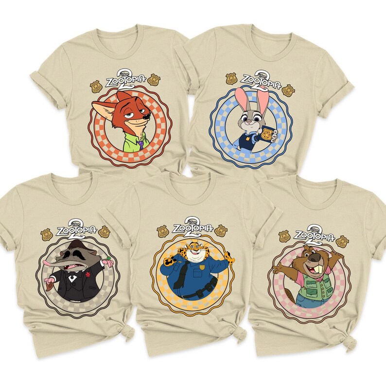 May include: Five beige t-shirts featuring characters from the animated film "Zootopia." Each shirt has a circular design with a different character, including a fox, rabbit, and others. The word "Zootopia" is printed above each character.