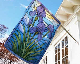 May include: A rectangular garden flag featuring a stained-glass design of purple iris flowers against a blue sky background. The flag is mounted on a metal pole and displayed outside a white house.