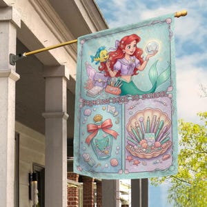 Puede incluir: Una bandera decorativa con Ariel de La Sirenita, con el texto "PRINCESS BACK TO SCHOOL". La bandera tiene un fondo azul claro con ilustraciones de &uacute;tiles escolares, conchas marinas y un frasco de perfume.
