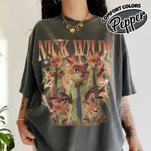 May include: A charcoal gray t-shirt featuring a graphic print of the character Nick Wilde in various poses. The text NICK WILDE appears in large orange letters above the character. Yellow lightning bolts surround the images. The shirt is labeled Pepper.