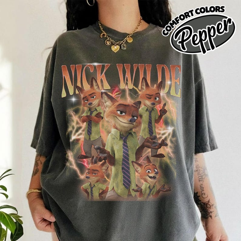 May include: A charcoal gray t-shirt featuring a graphic print of the character Nick Wilde in various poses. The text NICK WILDE appears in large orange letters above the character. Yellow lightning bolts surround the images. The shirt is labeled Pepper.